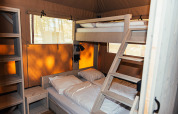 Vista interior de la tienda Safari + sanitario en Eurocamping Vessem BV, con literas y estanterías de madera.