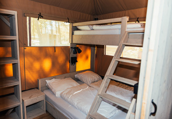 Vista interior de la tienda Safari + sanitario en Eurocamping Vessem BV, con literas y estanterías de madera.