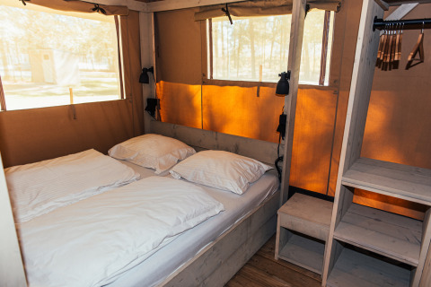 Inde i et Safari-telt med dobbeltseng, hylder og brede vinduer på Eurocamping Vessem BV i Holland.