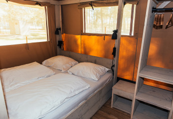 Interior de una tienda safari con cama doble, estanterías y ventanas en Eurocamping Vessem BV en Países Bajos.