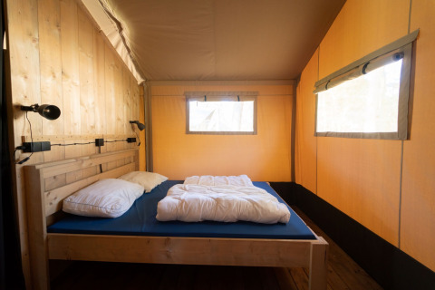 Vista interna di una tenda safari con letto in legno, biancheria e grandi finestre a Eurocamping Vessem BV.