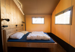 Vista interna di una tenda safari con letto in legno, biancheria e grandi finestre a Eurocamping Vessem BV.
