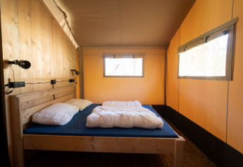 Vista interna di una tenda safari con letto in legno, biancheria e grandi finestre a Eurocamping Vessem BV.