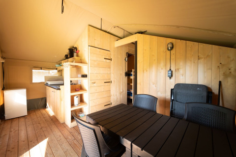 Interior view of a Safari tent lodge with kitchen, dining table, and wood panels at Eurocamping Vessem BV.