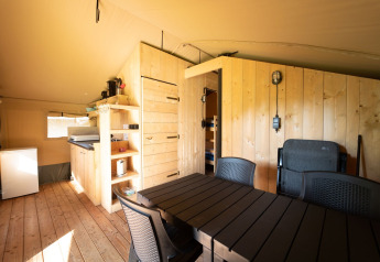 Interior view of a Safari tent lodge with kitchen, dining table, and wood panels at Eurocamping Vessem BV.