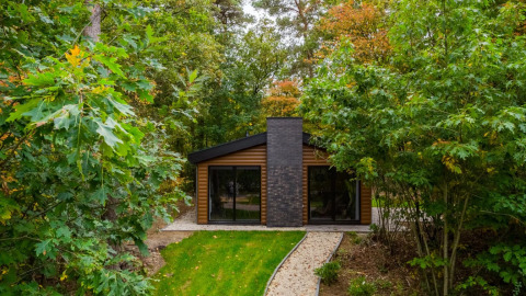 Cabane de glamping moderne entourée d’arbres verts dans un parc de vacances, idéale pour un séjour en nature.
