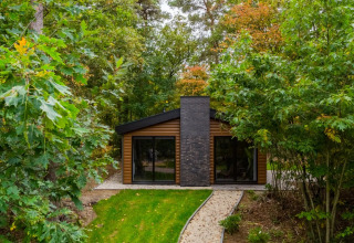 Modern glamping cabin nestled among lush trees at a holiday park, perfect for a peaceful nature getaway.