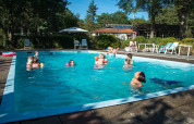 Familien und Kinder schwimmen im Pool eines Ferienparks mit Glamping-Unterkünften an einem sonnigen Tag.