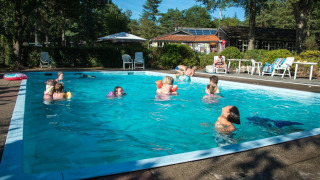 Niños y adultos disfrutan en la piscina de un parque vacacional con alojamientos de glamping al aire libre.