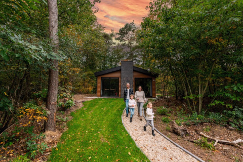 Familie spaziert einen Weg vor einer modernen Hütte im Wald entlang, Sonnenuntergang, Glamping-Urlaub.