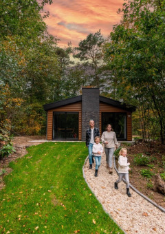Familia pasea por un sendero frente a una cabaña moderna en el bosque al atardecer en parque de glamping.