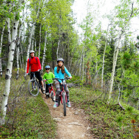 Una familia anda en bicicleta por un sendero boscoso en un parque vacacional con glamping.