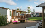 Acogedoras cabañas con terrazas de madera y tumbonas en un tranquilo camping rodeado de césped.