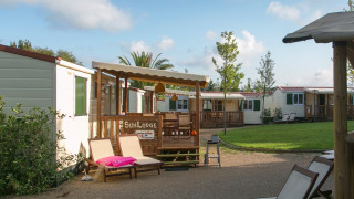 Acogedoras cabañas con terrazas de madera y tumbonas en un tranquilo camping rodeado de césped.
