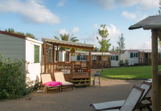 Cozy cabins with wooden decks and loungers in a peaceful, green camping site under a blue sky.