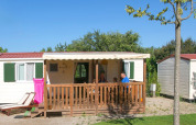 Een familie zit op het terras van een wit chalet met groene luiken en een roze luchtmatras buiten.