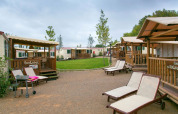 Zonnige lodges en ligzetels bij SunLodge Aspen Combi op Camping Vilanova Park, Spanje, met bewolkte lucht.