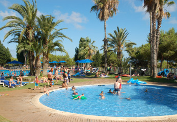 Famiglie si rilassano in una piscina circondata da palme in un glamping, bambini che si divertono in acqua.