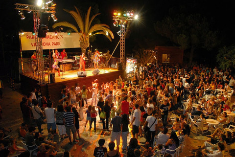 Nighttime concert and dancing at a glamping site with stage, live band, and a lively audience.
