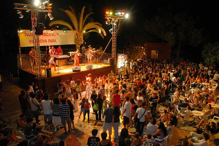Concierto nocturno y baile en un glamping con escenario, banda en vivo y numerosos asistentes.