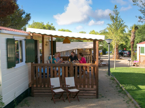 Famiglia cena sulla veranda della cabina SunLodge Redwood circondata da aree verdi e natura.