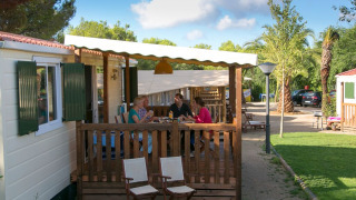 Famiglia cena sulla veranda della cabina SunLodge Redwood circondata da aree verdi e natura.
