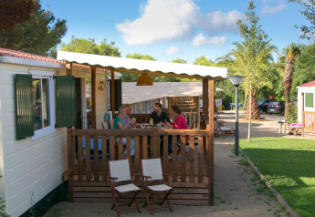 Famiglia cena sulla veranda della cabina SunLodge Redwood circondata da aree verdi e natura.