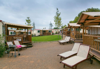 Bungalow SunLodge Redwood con lettini prendisole e prato verde a Camping Vilanova Park in Spagna.