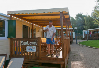 Hombre barriendo el porche de una cabaña SunLodge Redwood en el Camping Vilanova Park en España, día soleado.