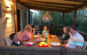 A family enjoys dinner together on a covered porch at a lodge, surrounded by nature in the evening.