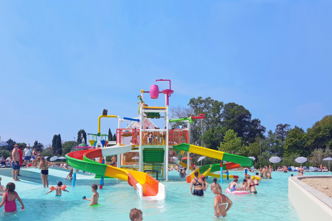 Niños y adultos se divierten en un colorido parque acuático con toboganes y piscinas al aire libre.