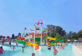 Bambini e adulti si divertono in un colorato parco acquatico con scivoli e piscine all'aperto.