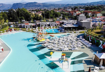 Aerial view of a holiday lodge with swimming pool, sun loungers, and mountain scenery in the background.