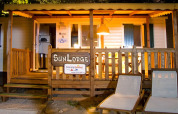 Evening view of SunLodge Maple at Camping Cisano/San Vito in Italy with deck chairs and an illuminated porch.