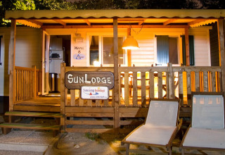Vista serale di SunLodge Maple al Camping Cisano/San Vito in Italia, con sdraio e veranda illuminata.