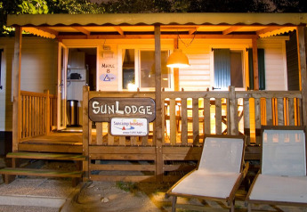 Vista nocturna de SunLodge Maple en Camping Cisano/San Vito, Italia, con tumbonas y porche iluminado.