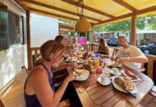 En familie spiser morgenmad sammen på terrassen ved en SunLodge Maple, omgivet af feriehytter.