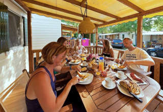 Familia desayunando junta en el porche de una SunLodge Maple, con cabañas de vacaciones alrededor.