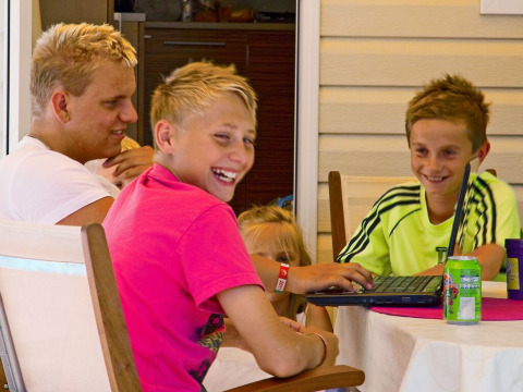 Cuatro niños se divierten en una mesa con un portátil en SunLodge Maple, Camping Cisano/San Vito, Italia.