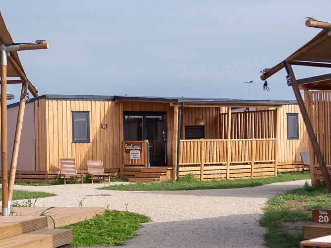 Foto van SunLodge Catalpa, een modern houten lodge met veranda, stoelen en grindpad in het park.