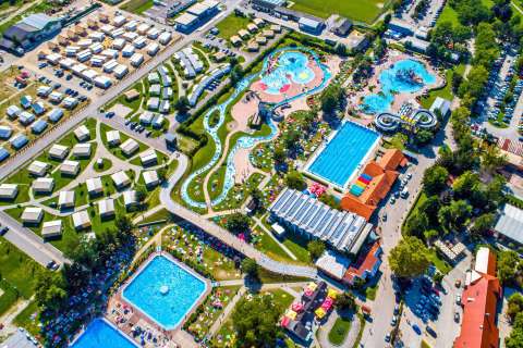 Vue aérienne d'un hébergement glamping avec tentes luxueuses, piscines, toboggans aquatiques et pelouses.