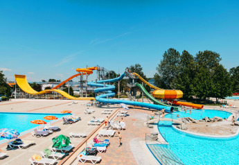 Waterpretpark met kleurrijke glijbanen, zwembaden en ligzetels onder parasols op een zonnige dag.
