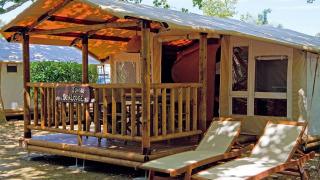 Alojamiento tipo tienda SunLodge Jungle con terraza, muebles de madera y dos tumbonas bajo árboles.