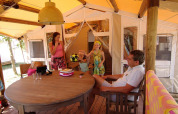 Famiglia che si rilassa e gioca con una palla sulla veranda di una tenda SunLodge Jungle in vacanza.