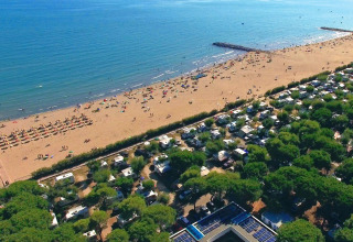 Foto aerea di una spiaggia sabbiosa con ombrelloni e campeggio vicino, circondati da alberi verdi.