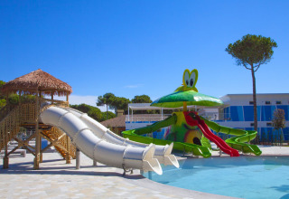 Zona acuática infantil con toboganes y decoración divertida junto a un albergue bajo cielo azul.