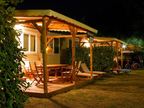 Nighttime photo of a cozy lodge with a wooden deck, outdoor furniture, and warm ambient lighting.
