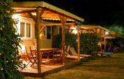 Foto nocturna de un lodge acogedor con terraza de madera, muebles de exterior y luz ambiental cálida.