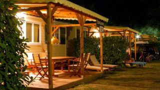 Nighttime photo of a cozy lodge with a wooden deck, outdoor furniture, and warm ambient lighting.