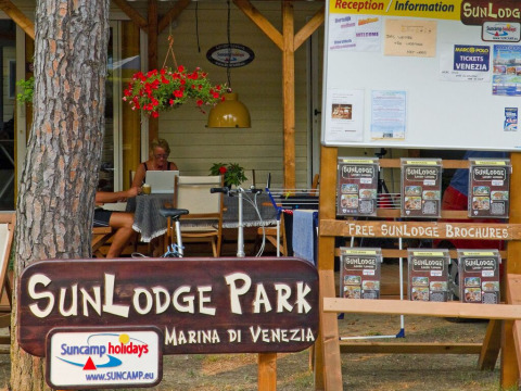 Área de recepción e información en SunLodge Park, Marina di Venezia, Italia, con folletos y visitantes.